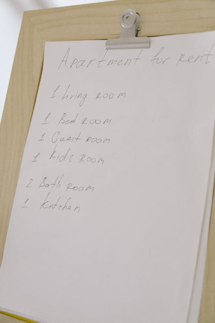 A whiteboard or paper with handwritten notes listing rooms in an apartment for rent, including a living room, bedroom, guest room, kids' room, two bathrooms, and a kitchen. The surface appears clean a
