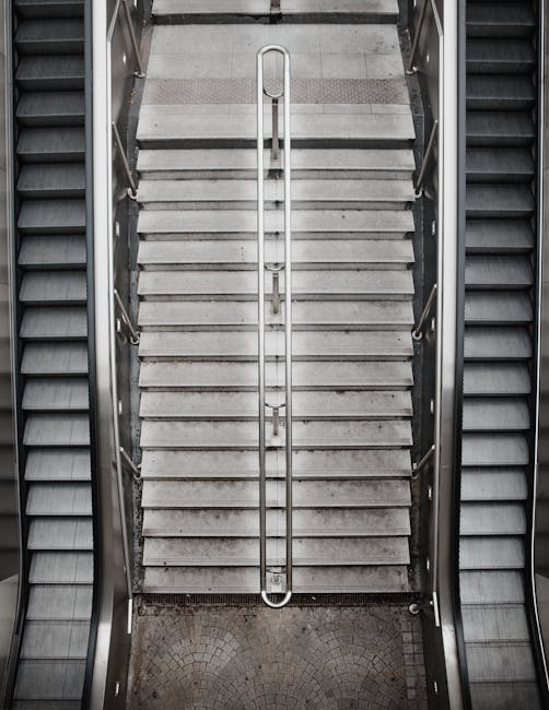 The image depicts a modern, multi-story concrete staircase with black metal railings, situated in a well-lit, indoor setting. The staircase has clean, white-painted surfaces showing a smooth finish, a